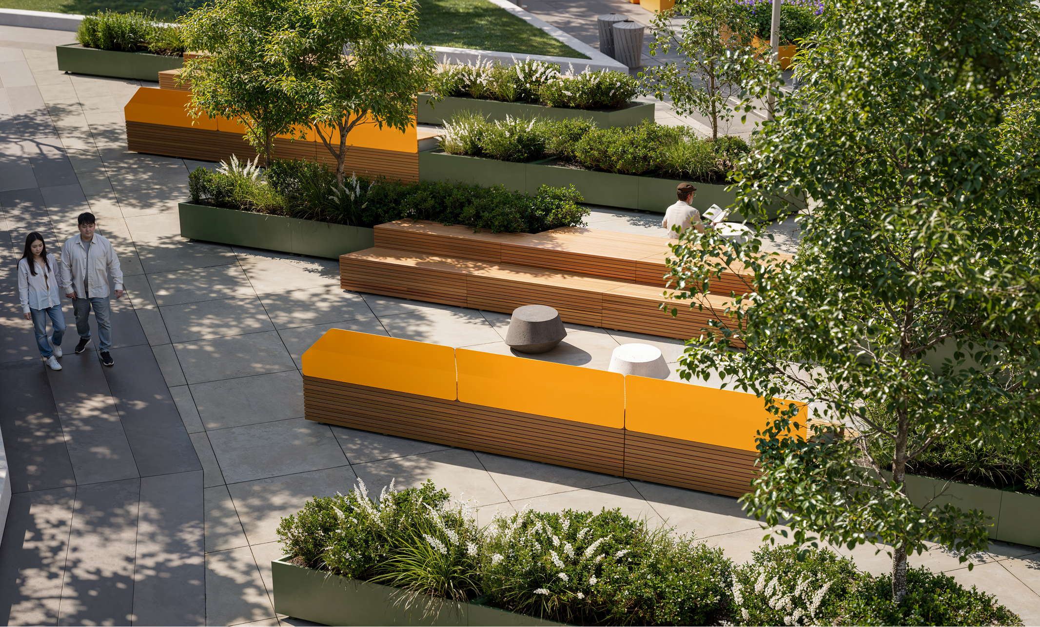 Modern urban park with benches, trees, and people walking.