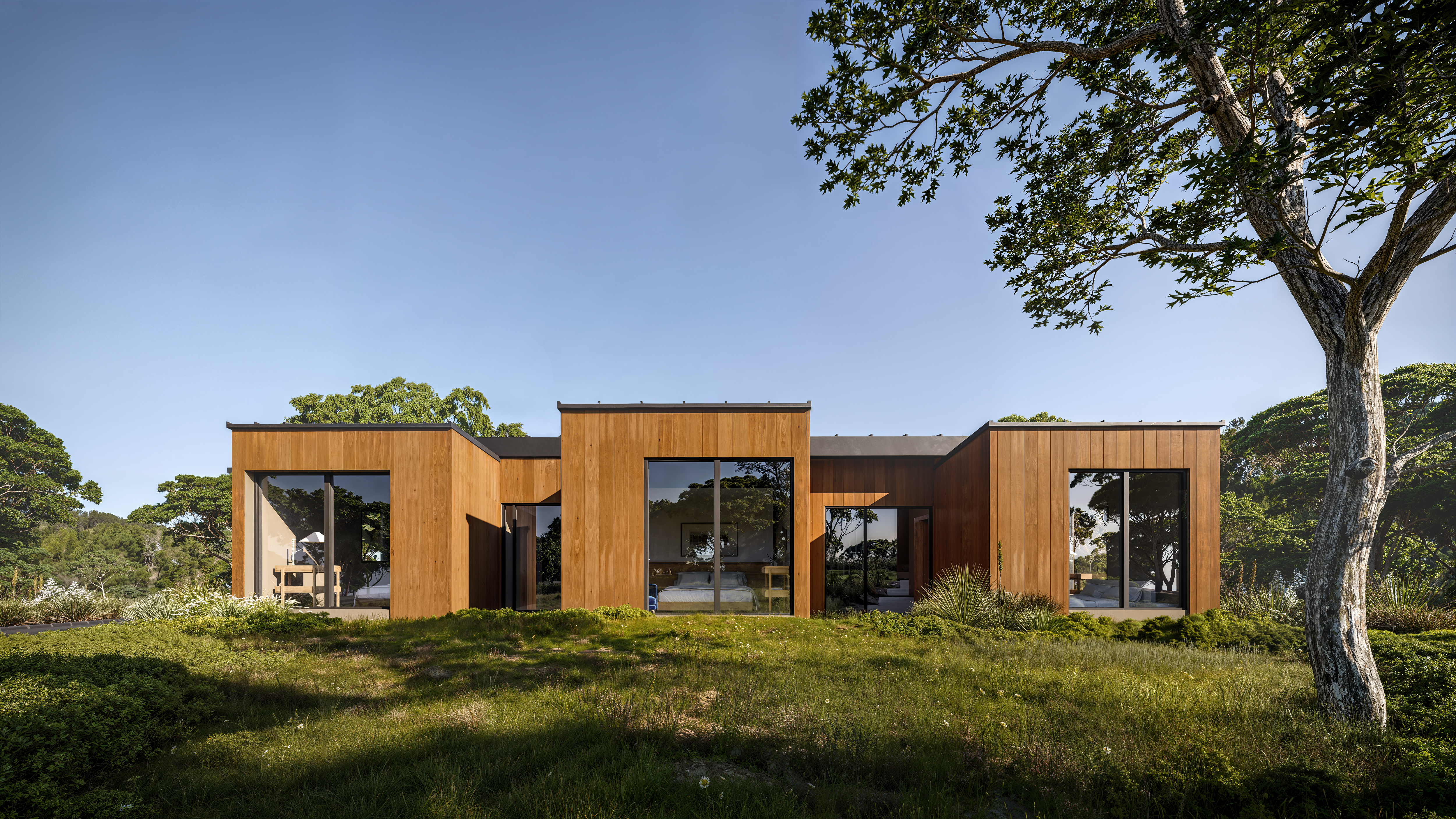 Modern wood home with large windows on a grassy hill.